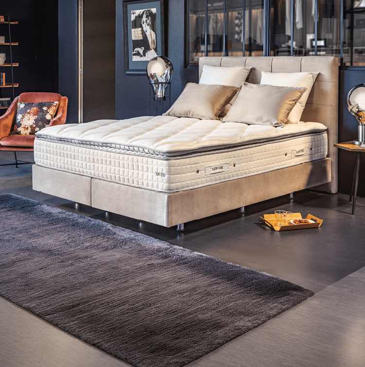 Un lit moderne avec un matelas pais et deux coussins est pos  sur un cadre beige avec un tapis gris fonc  devant dans une chambre  l gante.  Description g n r e par IA